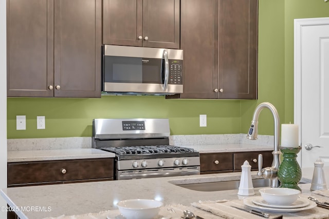 kitchen with stainless steel appliances, light stone countertops, dark brown cabinets, and sink