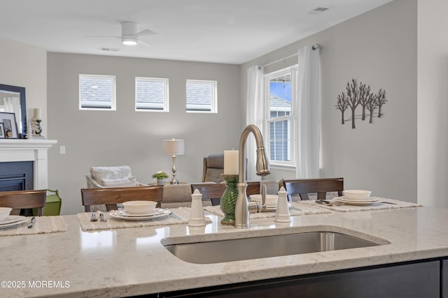 kitchen featuring ceiling fan, sink, and light stone counters