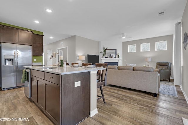 kitchen featuring sink, dark brown cabinets, appliances with stainless steel finishes, a kitchen island with sink, and light hardwood / wood-style floors