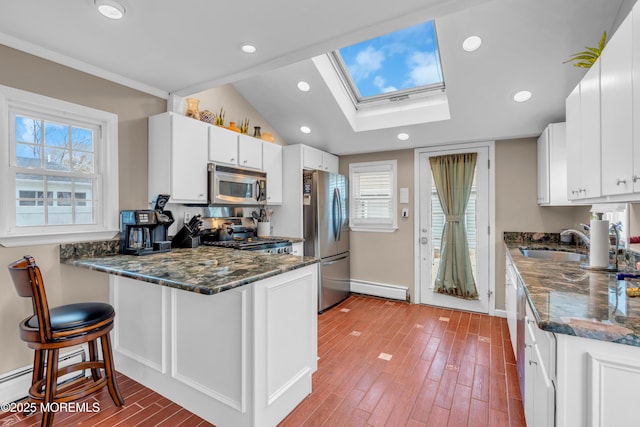 kitchen with sink, white cabinets, a kitchen bar, a baseboard heating unit, and stainless steel appliances