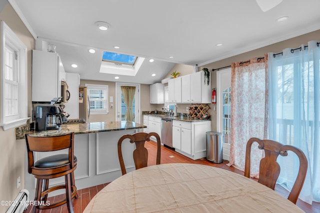 kitchen with appliances with stainless steel finishes, a baseboard radiator, dark stone countertops, white cabinets, and light hardwood / wood-style floors