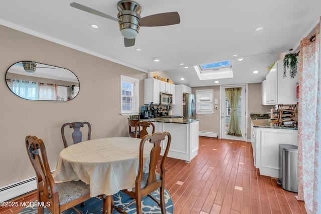 dining room featuring ceiling fan, vaulted ceiling with skylight, light wood-type flooring, and a baseboard heating unit