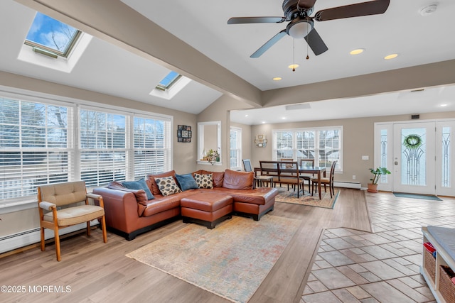 living room featuring ceiling fan, vaulted ceiling with skylight, light hardwood / wood-style floors, and a wealth of natural light