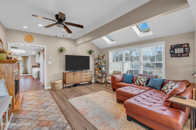 living room featuring ceiling fan, vaulted ceiling with skylight, and light hardwood / wood-style flooring