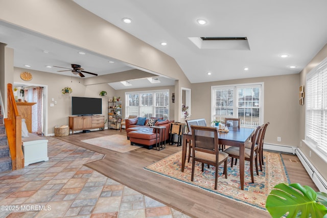 dining room with ceiling fan, a baseboard radiator, vaulted ceiling with skylight, and light hardwood / wood-style flooring