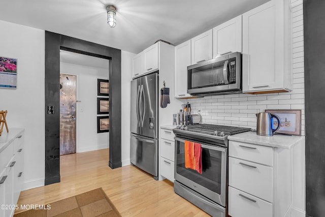 kitchen with appliances with stainless steel finishes, tasteful backsplash, white cabinets, light stone countertops, and light hardwood / wood-style flooring