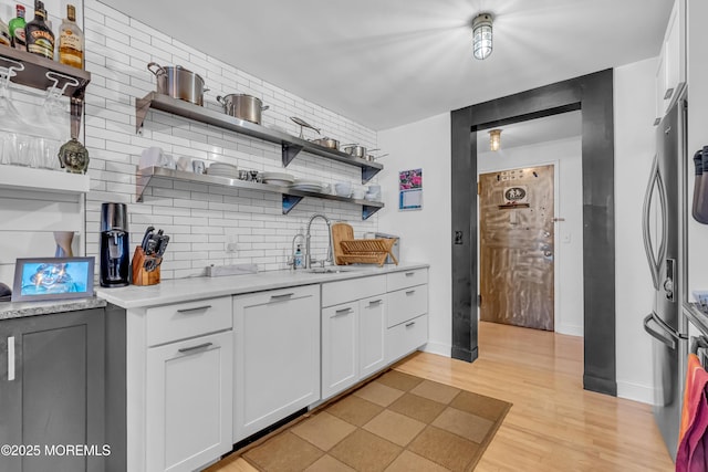 kitchen with sink, stainless steel fridge, tasteful backsplash, white cabinets, and light wood-type flooring