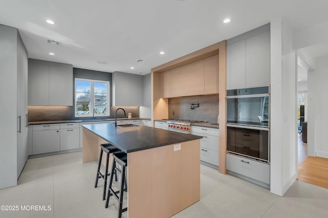 kitchen featuring sink, tasteful backsplash, a kitchen breakfast bar, gray cabinets, and an island with sink