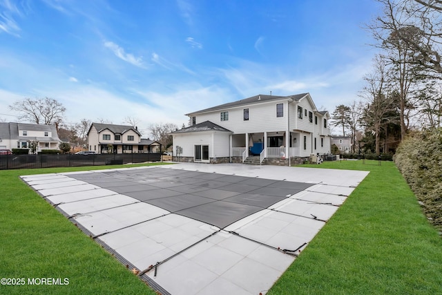 rear view of house with a patio area, a covered pool, and a lawn