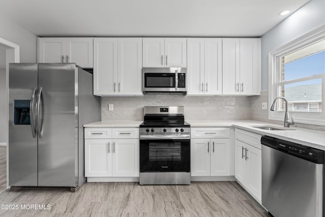 kitchen featuring sink, stainless steel appliances, white cabinets, decorative backsplash, and light wood-type flooring