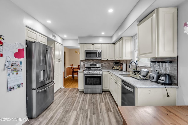 kitchen with appliances with stainless steel finishes, sink, white cabinets, and light wood-type flooring