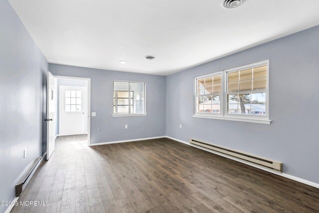 spare room featuring dark wood-style floors, baseboard heating, visible vents, and a healthy amount of sunlight