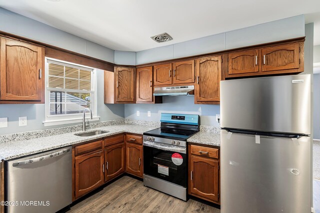 kitchen featuring appliances with stainless steel finishes, brown cabinetry, a sink, and under cabinet range hood