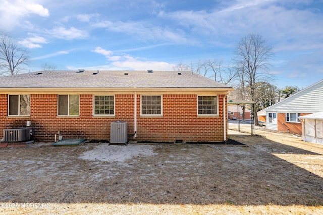 rear view of property featuring a shingled roof, central AC unit, a carport, and brick siding