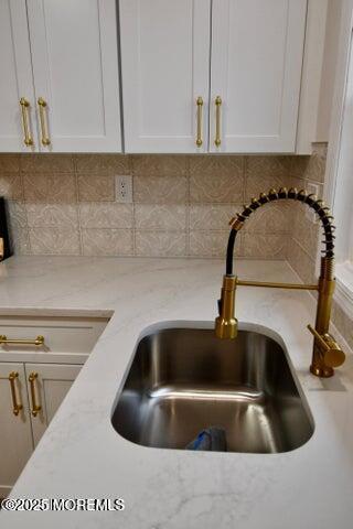 room details featuring light stone counters, white cabinetry, sink, and tasteful backsplash