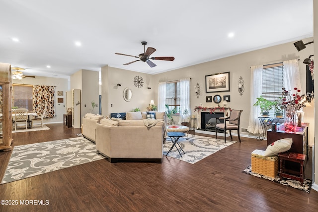 living room with a glass covered fireplace, wood finished floors, and a ceiling fan