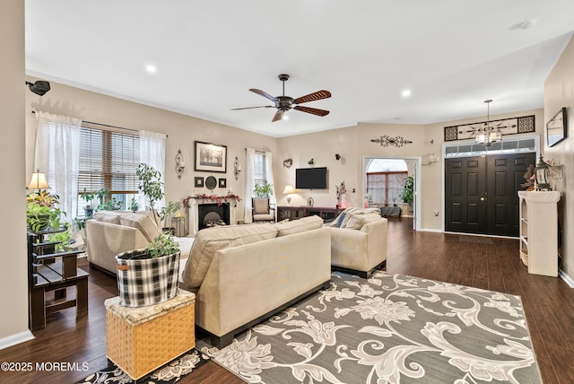 living area featuring ceiling fan with notable chandelier, a fireplace, wood finished floors, and baseboards