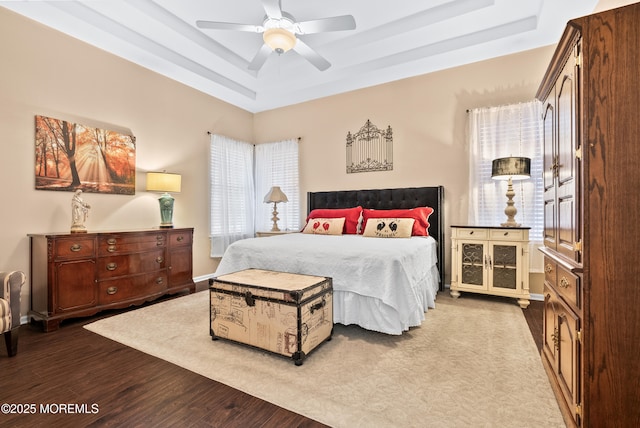 bedroom featuring ceiling fan, wood finished floors, a raised ceiling, and baseboards