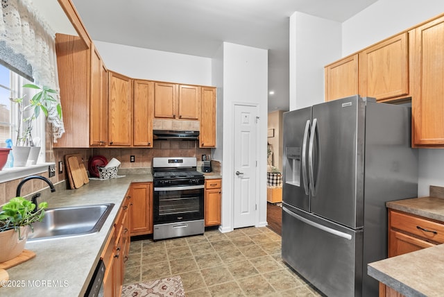 kitchen with a sink, stainless steel appliances, light countertops, under cabinet range hood, and backsplash