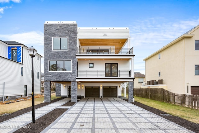 view of front facade featuring decorative driveway, fence, a balcony, a garage, and stone siding