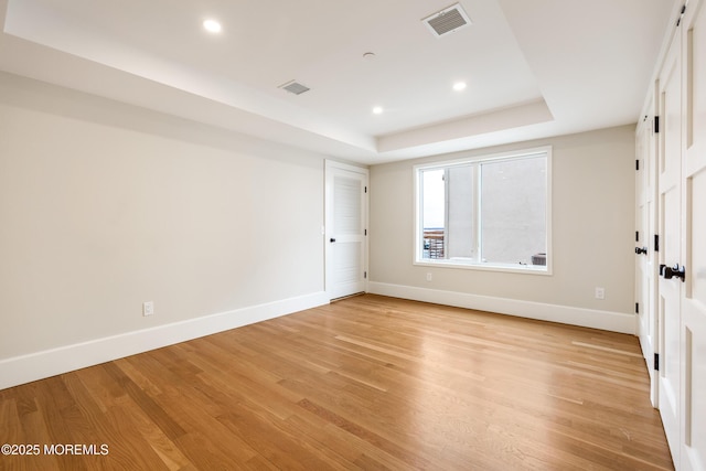 unfurnished bedroom with baseboards, visible vents, a raised ceiling, light wood-style floors, and recessed lighting