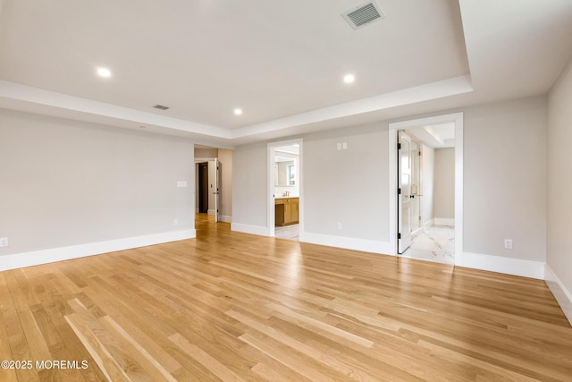 empty room featuring light wood finished floors, a tray ceiling, visible vents, and recessed lighting