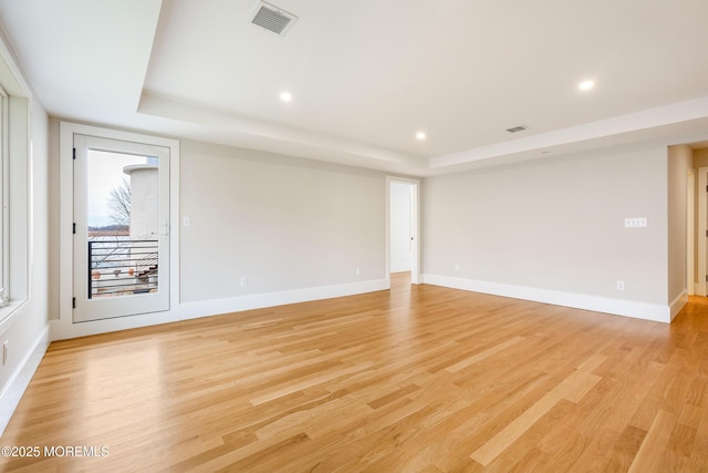 unfurnished room featuring light wood-style floors, baseboards, visible vents, and a tray ceiling