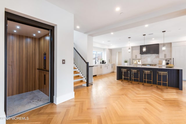 interior space featuring a center island, light countertops, hanging light fixtures, elevator, and a kitchen breakfast bar