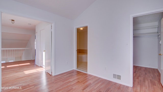 unfurnished bedroom with a walk in closet, vaulted ceiling, a closet, and light hardwood / wood-style flooring