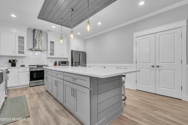 kitchen with wall chimney range hood, appliances with stainless steel finishes, hanging light fixtures, a center island, and white cabinets