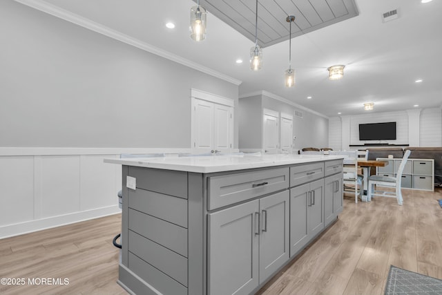 kitchen with crown molding, gray cabinets, light stone countertops, a kitchen island, and decorative light fixtures