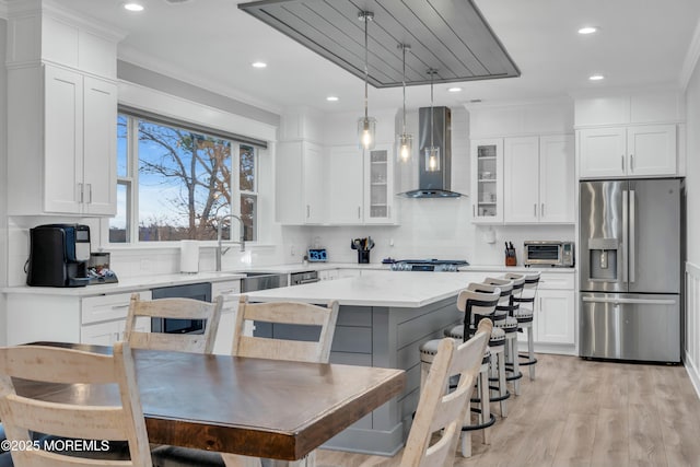 kitchen with a kitchen island, white cabinetry, stainless steel fridge, hanging light fixtures, and wall chimney exhaust hood