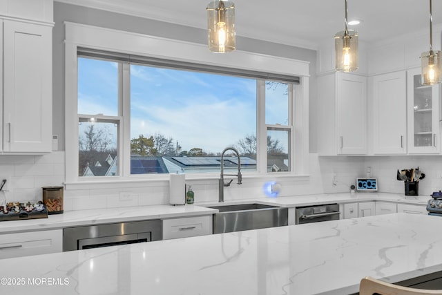 kitchen with sink, white cabinetry, hanging light fixtures, ornamental molding, and light stone countertops