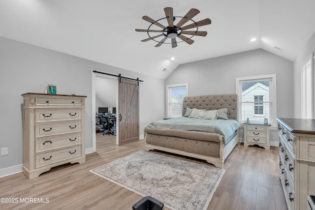 bedroom featuring a barn door, light hardwood / wood-style floors, vaulted ceiling, and multiple windows