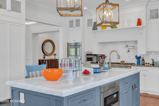 kitchen featuring pendant lighting, white cabinetry, appliances with stainless steel finishes, and a kitchen island with sink