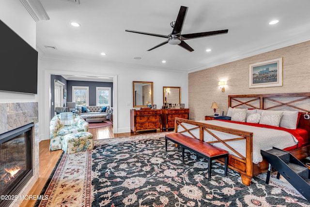 bedroom with hardwood / wood-style floors, crown molding, and a high end fireplace