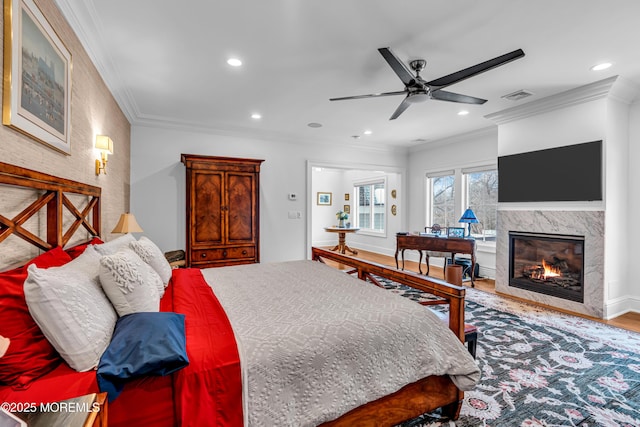 bedroom featuring hardwood / wood-style flooring, ornamental molding, ceiling fan, and a high end fireplace