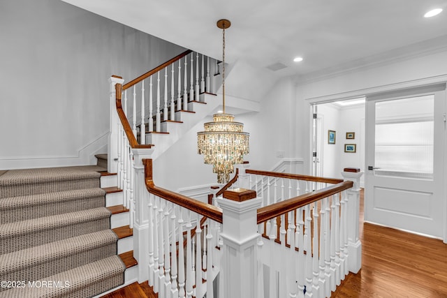 staircase with hardwood / wood-style flooring, ornamental molding, and a chandelier