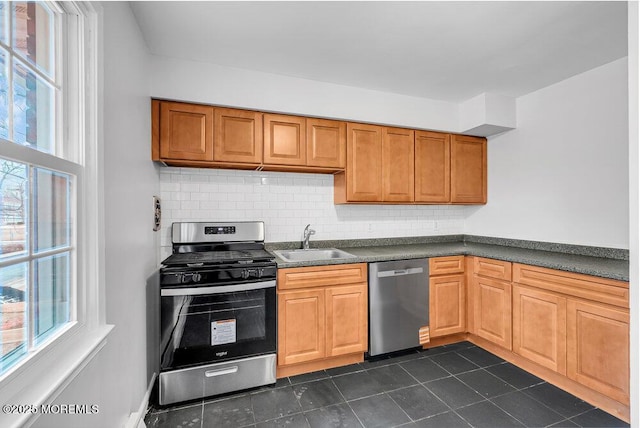 kitchen with appliances with stainless steel finishes, dark tile patterned flooring, sink, and backsplash