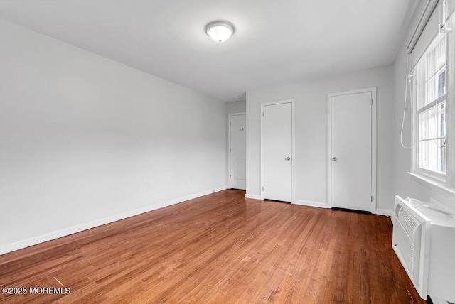 unfurnished bedroom featuring wood-type flooring, radiator, and two closets