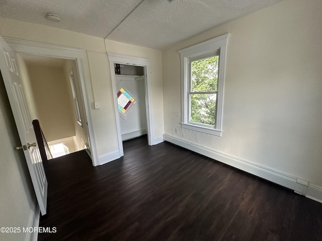 unfurnished bedroom with a baseboard heating unit, a textured ceiling, dark hardwood / wood-style floors, and a closet