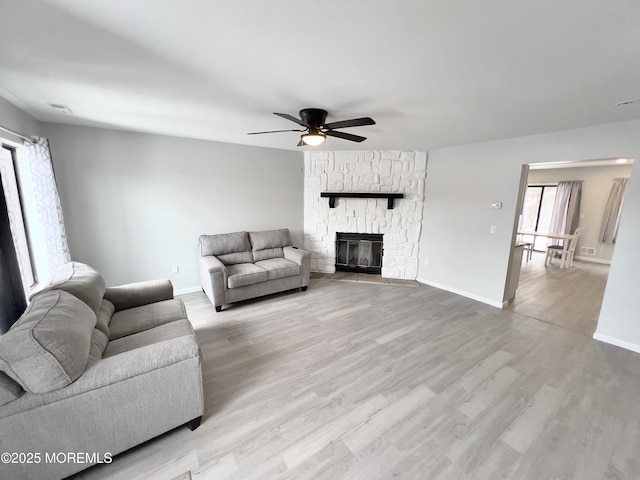 living room with ceiling fan, a stone fireplace, and light hardwood / wood-style floors