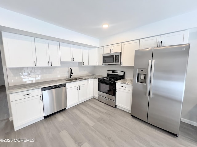 kitchen featuring sink, white cabinets, stainless steel appliances, light stone countertops, and light hardwood / wood-style flooring