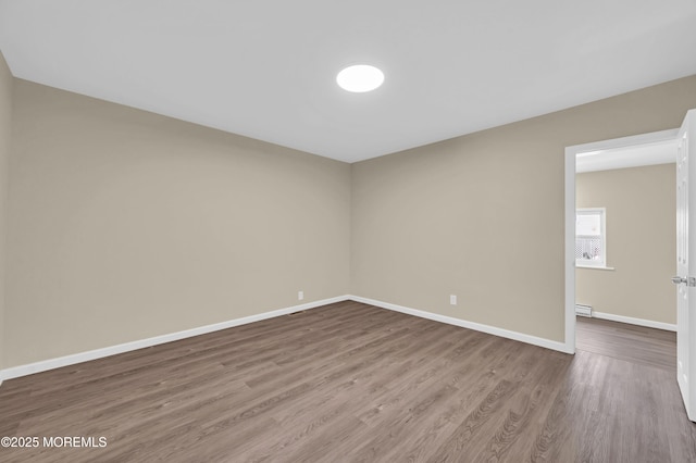 unfurnished room with a baseboard heating unit and hardwood / wood-style floors