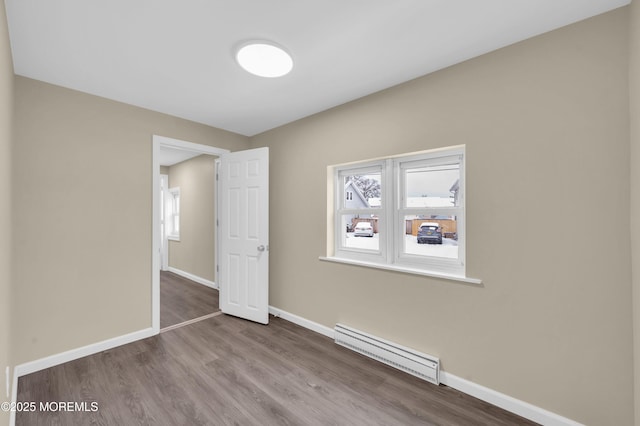 unfurnished room featuring baseboard heating, wood-type flooring, and a wealth of natural light