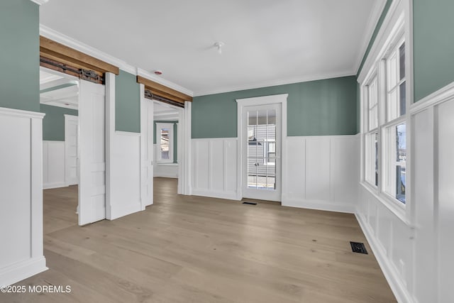 unfurnished room featuring ornamental molding, a barn door, and light hardwood / wood-style flooring