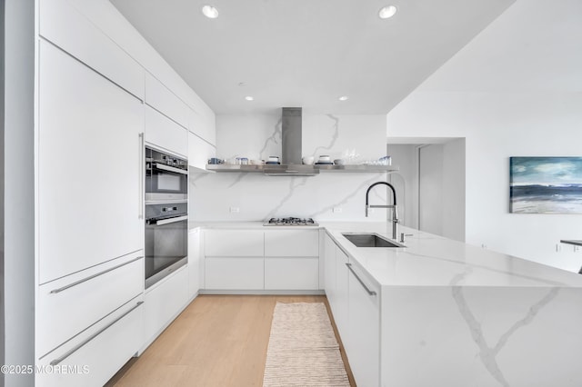 kitchen with appliances with stainless steel finishes, light stone countertops, island exhaust hood, sink, and white cabinetry