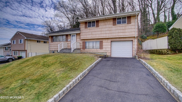 split level home with aphalt driveway, an attached garage, a front lawn, and fence