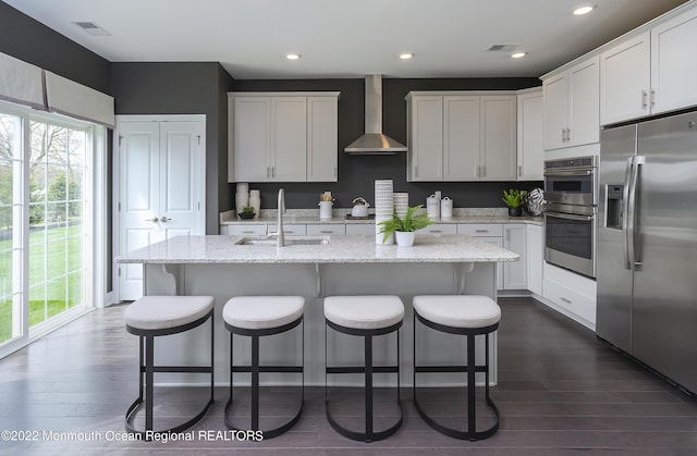 kitchen featuring an island with sink, stainless steel appliances, sink, and wall chimney range hood