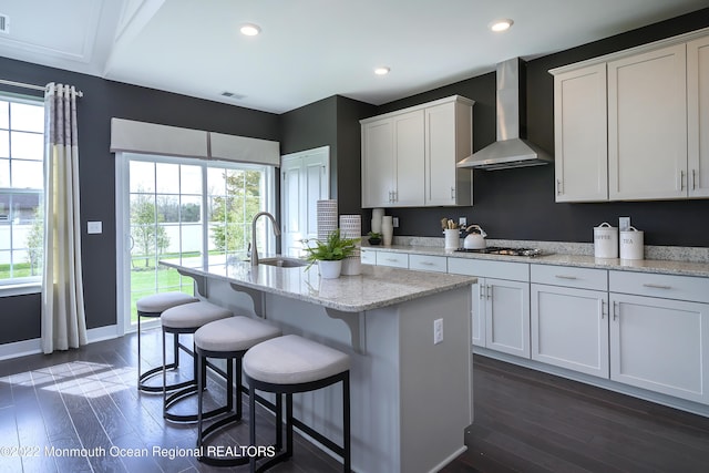 kitchen with white cabinetry, sink, wall chimney range hood, and a kitchen island with sink